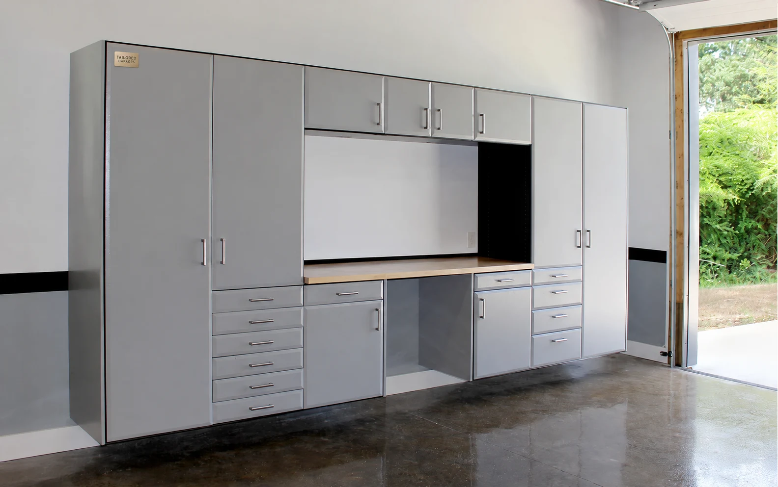 Wall-mounted gray garage cabinetry with tall storage, drawers, a wood worktop and a small Tailored Garages badge